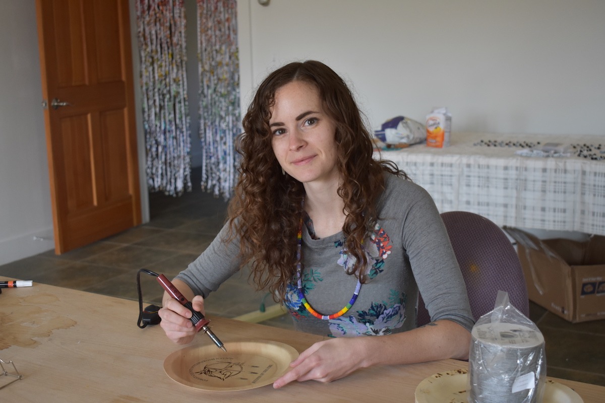 Sydney Purshell uses a woodburning tool to draw onto a wooden plate shaped piece