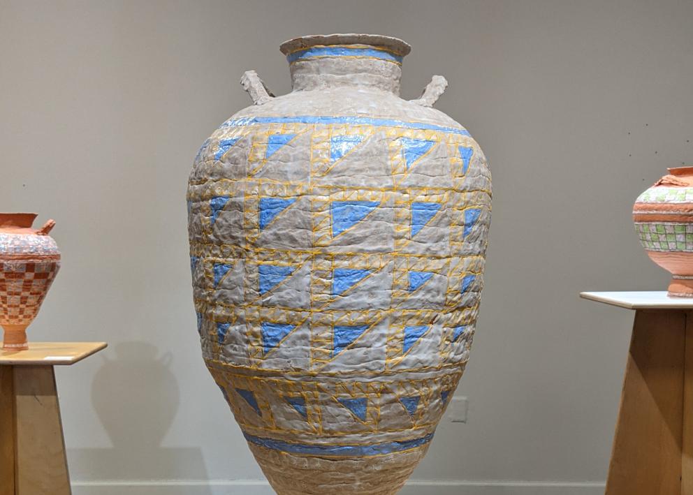 In the foreground, a bulbous vase with small handles adorned in a geometric pattern of blue and yellow. On either side similar vases sit in the background
