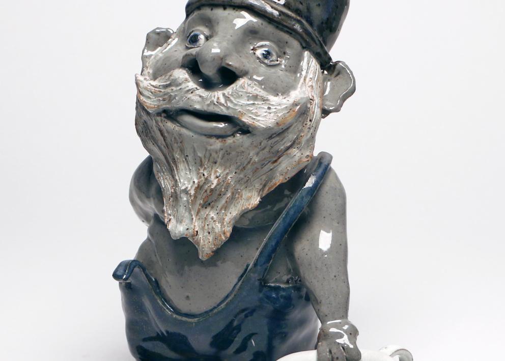 A blue grey ceramic gnome leans on a white teacup