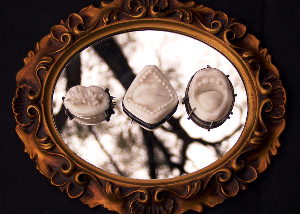 Three different cast mouths sit on an ornate mirror. The mouths are open, with teeth bared.