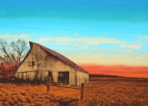 a barn sits in front of a blue sky with setting orange at the horizon.